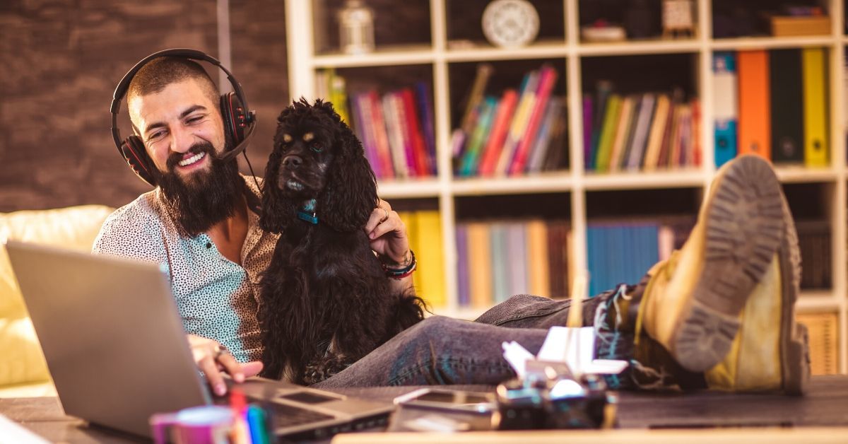 Call center agent answers call about pet insurance claim while working from home with his spaniel. 